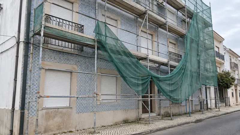 Andaime montado na fachada de azulejo de um prédio, sem ninguém a trabalhar e com a rede de protecção descaída