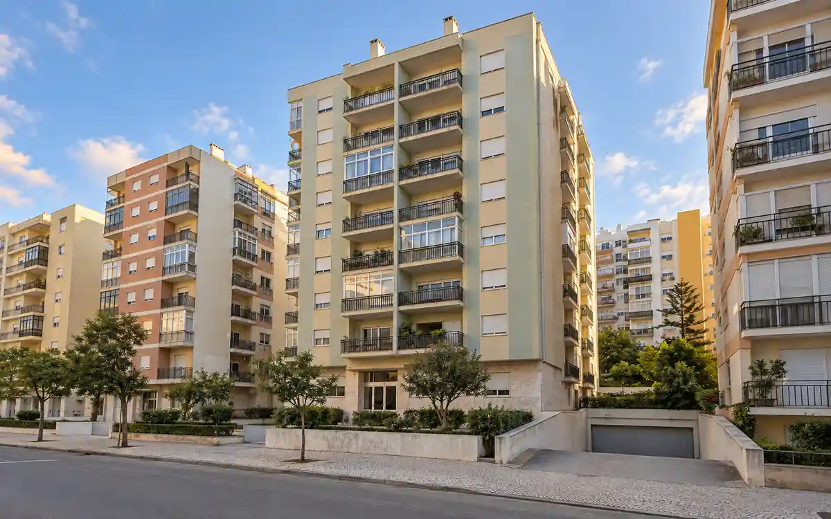 Imagem ilustrativa de uma rua da Cova da Piedade com prédios de habitação de oito a dez andares e a entrada de uma garagem colectiva