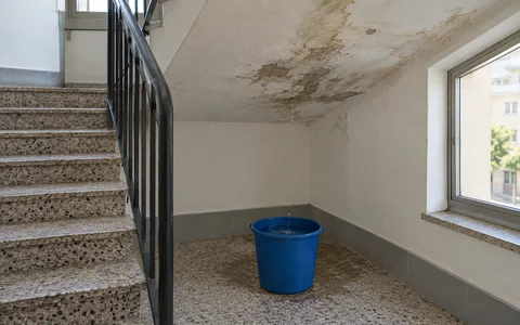 Balde a apanhar pingos de água no patamar da escada de um prédio, por baixo de uma mancha de humidade no tecto
