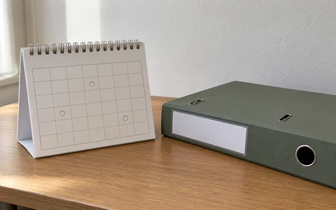 Calendário de secretária com datas marcadas e uma pasta de arquivo ao lado