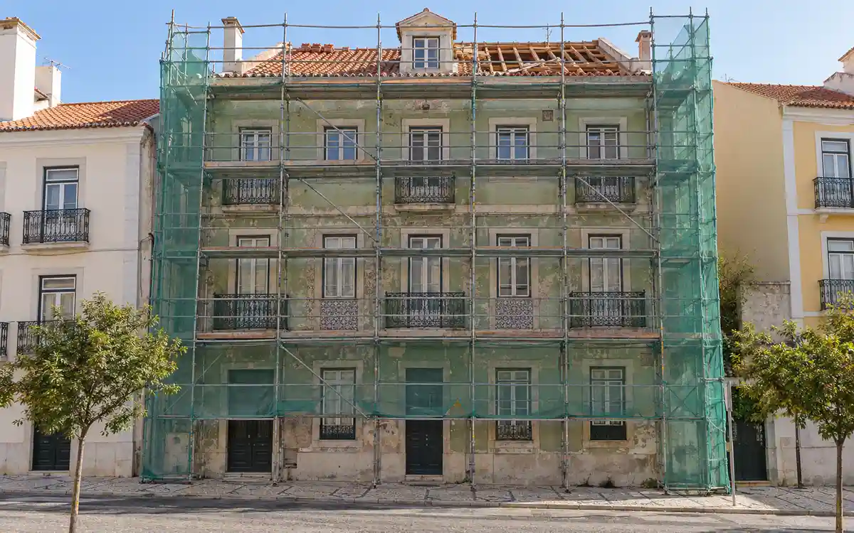 Imagem ilustrativa de um prédio antigo de Lisboa com andaimes na fachada e a cobertura em obra