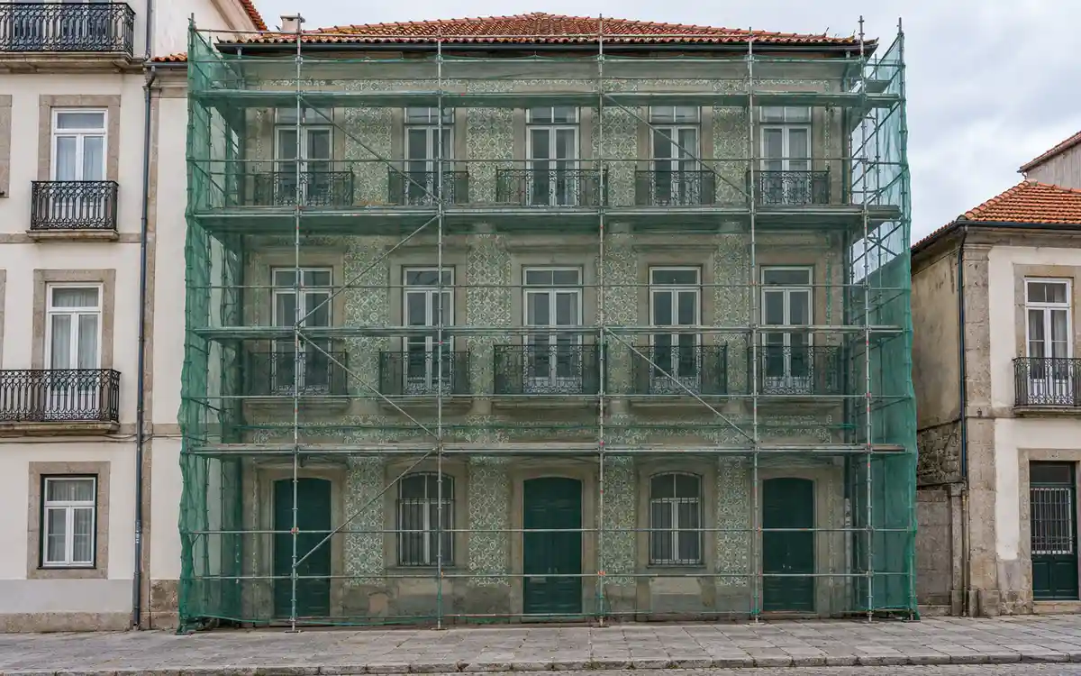 Imagem ilustrativa de um prédio antigo do Porto, de granito e azulejo, com andaime e rede na fachada