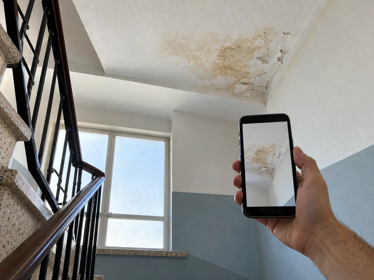 Tecto de uma caixa de escada com uma mancha de humidade, fotografado com um telemóvel