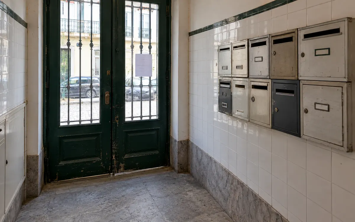Entrada de um prédio antigo de habitação, com caixas de correio de várias épocas e um aviso colado na porta