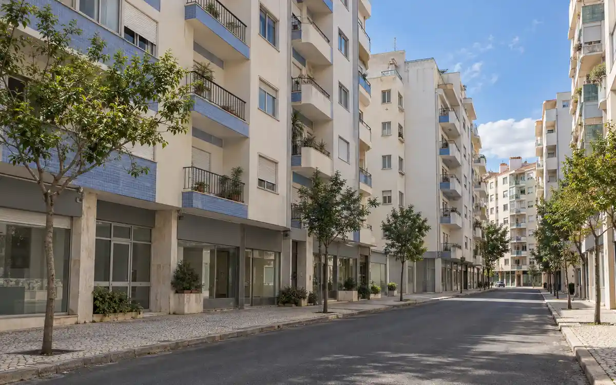 Imagem ilustrativa de uma rua de Queluz com prédios de habitação de seis a oito andares e lojas no rés-do-chão
